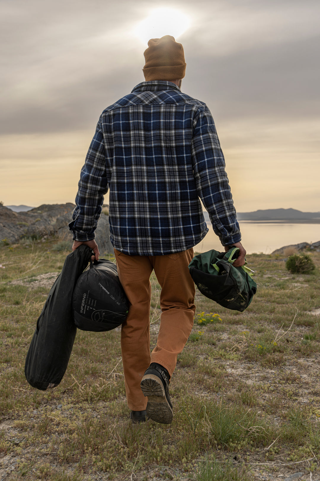 An adventurer, sporting Bulletprufe Jeans - Whiskey Denim Slim Fit, strides confidently with camping gear, ready for any ultimate outdoor experience.