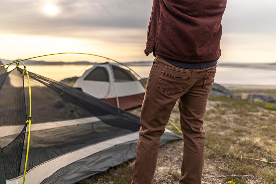 Man wearingTobacco Brown Adventure Fit - 6th Gen Bulletprufe Jeans, savoring a sunset view while camping in the great outdoors.