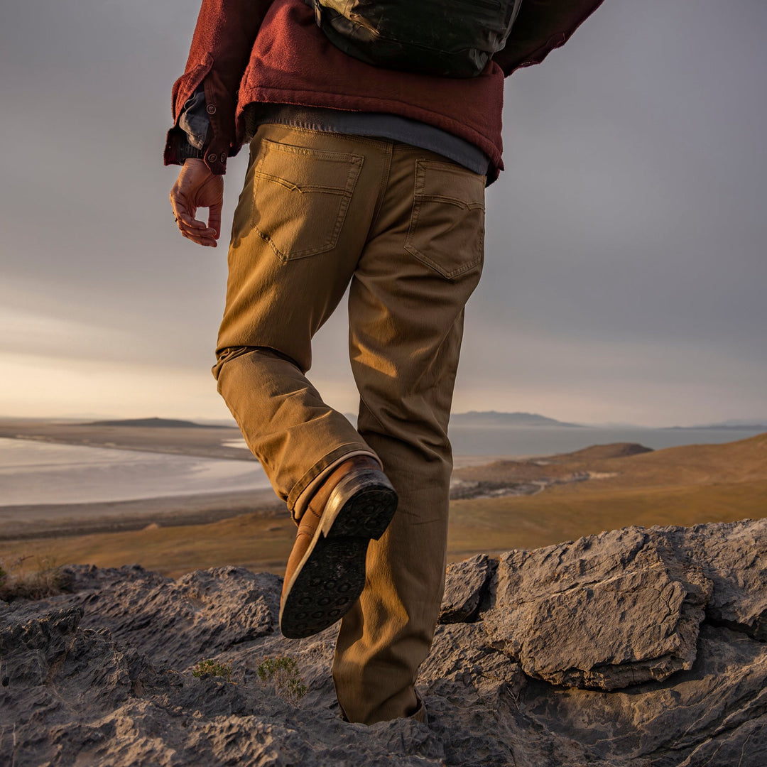 Man in Olive Green Kush Denim Jeans - Adventure Fit - 6th Gen, standing with a back view, gazing at a breathtaking outdoor horizon during an adventurous journey.