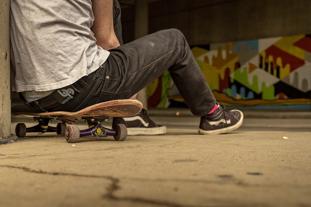A man comfortably seated on his skateboard while sporting Blackout Denim Slim Fit 6th Gen Bulletprufe Jeans. Escape the every day knowing that your jeans provide the utmost durability, comfort, and flexibility.