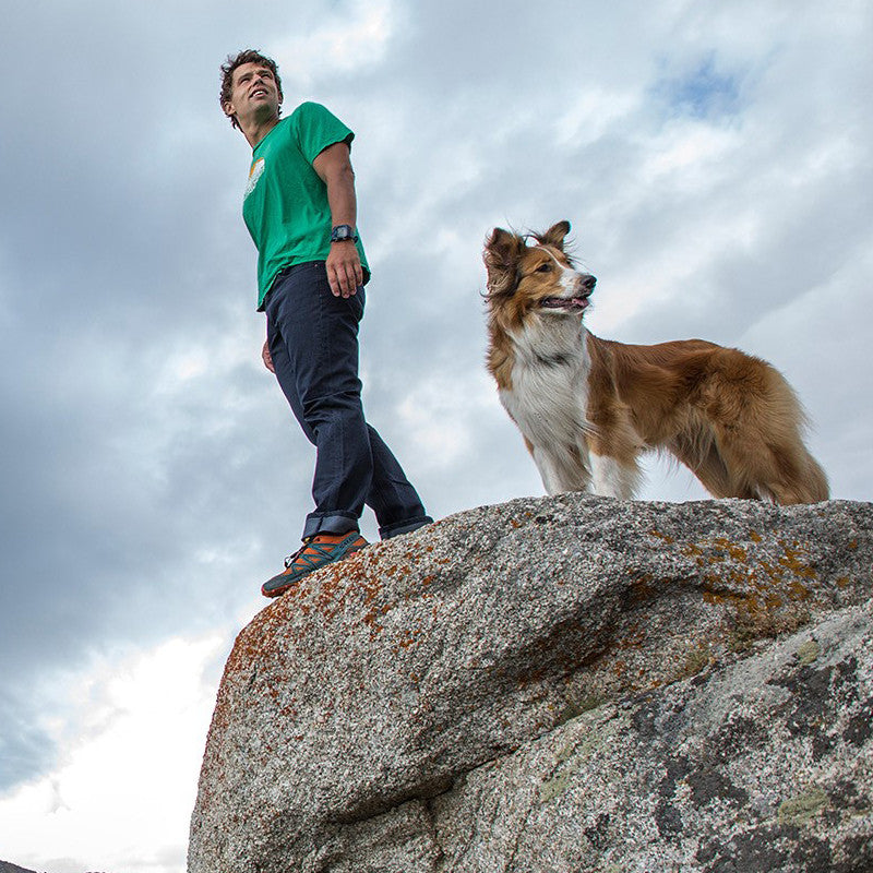 A man in Midnight Blue Denim - Slim Fit - 6th Gen stands beside a rock with his loyal dog, both immersed in the joy of an outdoor adventure.