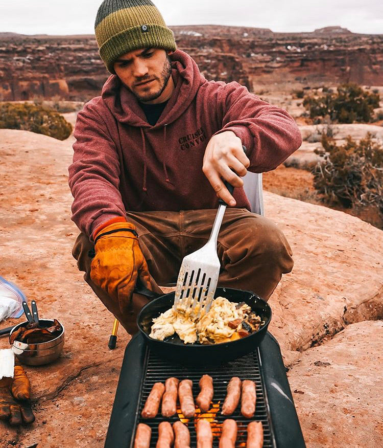 A man wearing a Tobacco Brown color Custom Waxed Tin-Cloth Bulletprufe is immersed in outdoor cooking.