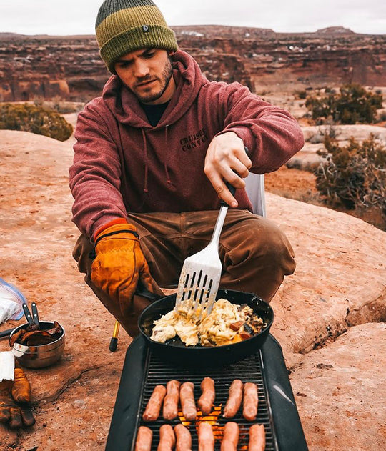 A man wearing a Tobacco Brown color Custom Waxed Tin-Cloth Bulletprufe is immersed in outdoor cooking.