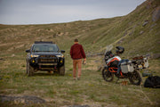 Man with off-road car and motorcycle, savoring the outdoor scenery in his Tobacco Brown Adventure Fit - 4th Gen Bulletprufe Jeans.