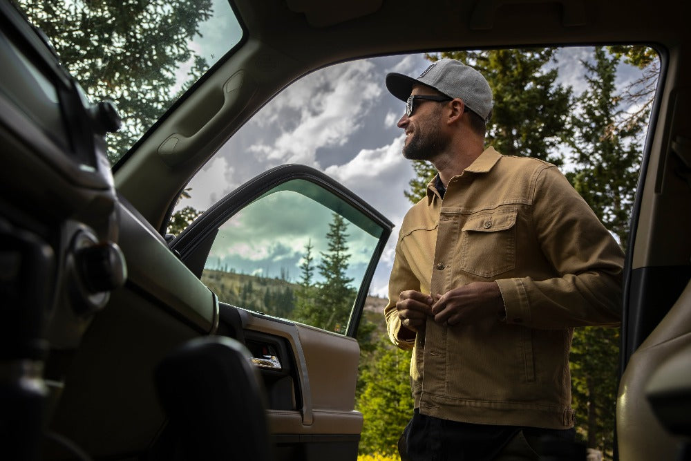 A man buttoning his Overland Jacket as he exits his vehicle getting ready to embark on the great outdoors. 