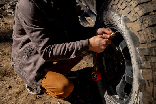 A man putting air in a tire wearing his new Overland Jacket as he gets ready for his next big adventure. 