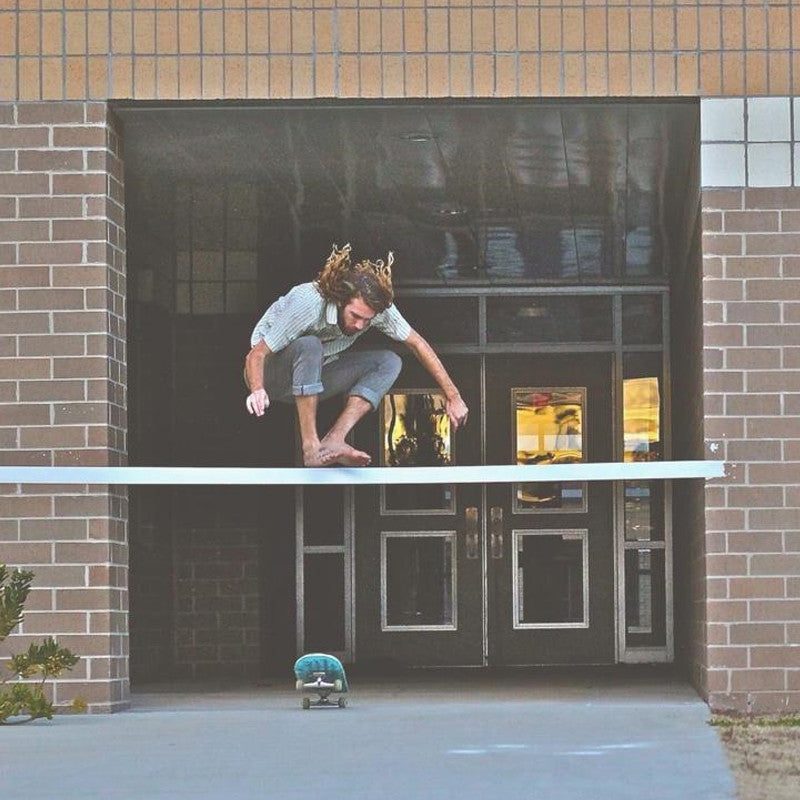 Skateboarder executing an impressive jump stunt, sporting a sleek look in Slate Gray Slim Fit Denim - 6th Gen jeans.