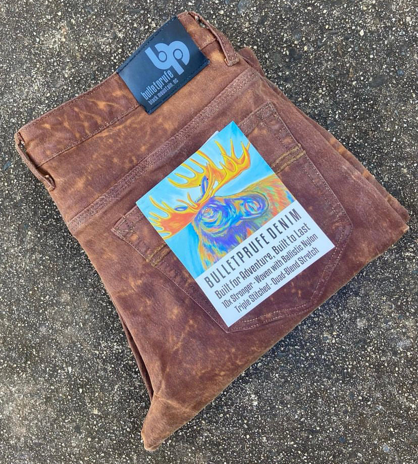 Whiskey Bulletprufe Custom Waxed Tin-Cloth laid out in an outdoor adventure setting. Built to withstand the elements, each pair is hand-waxed and finished, and will last a lifetime.